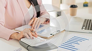 Young businesswoman analyzes cost graphs on desk in conference room with laptop