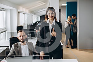 Young businesswoman and businessman working together in office. Beautiful office girl showing thumb up