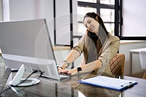 Young Businesswoman On Call While Using Computer At Desk