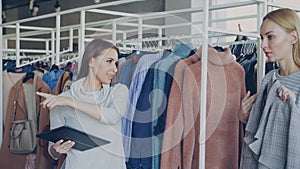 Young businesswoman is checking clothes in her store with tablet in hands. Her employee is coming and asking about