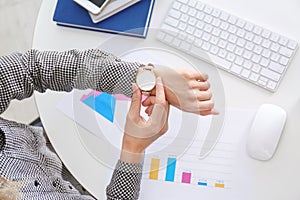 Businesswoman checking time on her wristwatch at workplace, top view. Time management