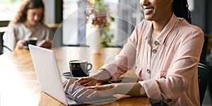 Young Businesswoman With Coffee Working On Laptop Sitting In Cafe Or Office With Colleague In Background