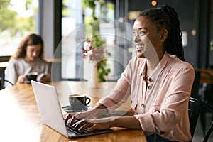 Young Businesswoman With Coffee Working On Laptop Sitting In Cafe Or Office With Colleague In Background