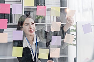 Young businesswoman creative team using post it notes in glass wall to writing strategy business plan to development