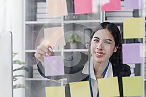 Young businesswoman creative team using post it notes in glass wall to writing strategy business plan to development