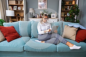 Young businesswoman cryptocurrency trader sitting in home office working on tablet while sitting on sofa. Freelance female global