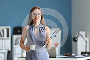 Young businesswoman with cup of coffee and clipboard in office