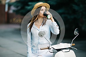 Young businesswoman drinking a coffee on a italian scooter. Woman standing at scooter on the street.