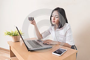 Young businesswoman drinking coffee while working with laptop at the desk. Coffee break at office concept