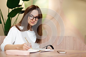 Young businesswoman in eyeglasses planning and writing down the daily schedule with in agenda