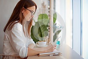 Young businesswoman in eyeglasses planning and writing down the daily schedule with in agenda