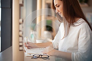 Young businesswoman in eyeglasses planning and writing down the daily schedule with in agenda