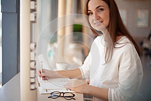 Young businesswoman in eyeglasses planning and writing down the daily schedule with in agenda