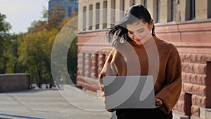 Young businesswoman freelancer student sitting outdoors reading email on laptop smiling laughing good news feels happy