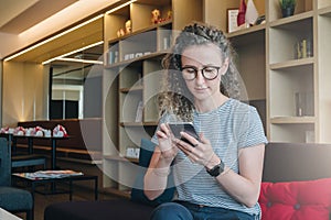 Young businesswoman in glasses sits, uses smartphone, working.