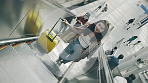 Young businesswoman going on escalator with suitcase in railroad station. Beautiful woman on a way for business working
