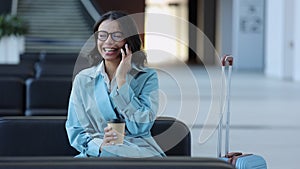 Young businesswoman having mobile call and laughing, sitting in airport and waiting for flight.