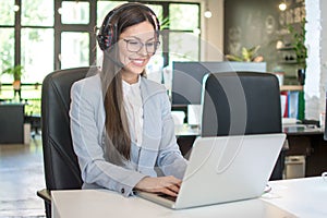 Young businesswoman with headset working on laptop in modern office