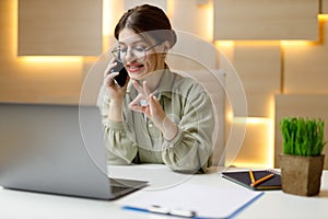 Young businesswoman at her workplace talking on the phone a successful deal. Shows a gesture ok, persuades the client photo