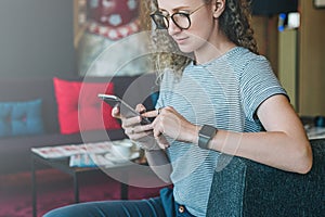 Young businesswoman hippest sits on sofa in hotel lobby and uses smartphone.Girl chatting,working,learning,shopping