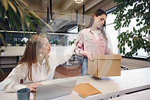 Young businesswoman holding box of personal belongings about to leave office after quitting job