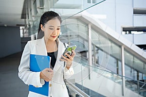 Young businesswoman holding document and using a smartphone while walking through the city