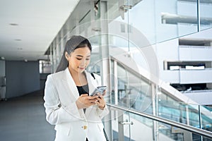 Young businesswoman holding document and using a smartphone while walking through the city