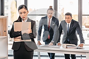 Young businesswoman holding folder and businessmen standing behind