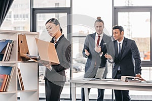 Young businesswoman holding folder while colleagues standing and looking behind