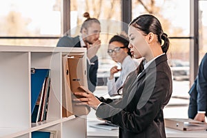 Young businesswoman holding folder while colleagues standing and looking behind