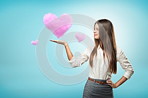 Young businesswoman holding pink cloud heart on her hand on blue background