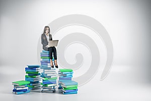 Young businesswoman with laptop sitting on colored books