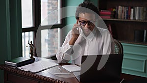 Young businesswoman lawyer talking on phone and looking at laptop, sitting at table in office spbas.