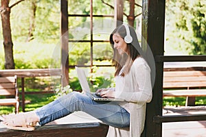 Young businesswoman in light casual clothes. Woman working on modern laptop pc computer, listen music in headphones on