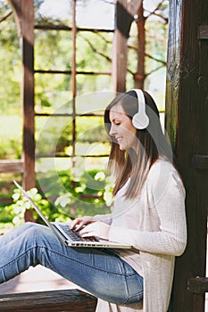Young businesswoman in light casual clothes. Woman working on modern laptop pc computer, listen music in headphones on