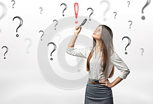 Young businesswoman with magnifying glass over her head looking at red exclamation mark surrounded by question marks