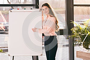 Young businesswoman making presentation in blank whiteboard and looking at camera