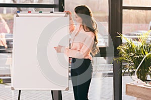 Young businesswoman making presentation and pointing at blank whiteboard