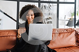 Young businesswoman making purchase with laptop and credit card at home