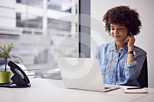 Young Businesswoman In Modern Office Working On Laptop Using Wireless Earpiece