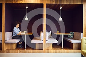 Young Businesswoman In Modern Open Plan Office Working On Laptop In Seating Pod