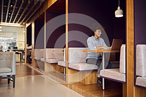 Young Businesswoman In Modern Open Plan Office Working On Laptop In Seating Pod