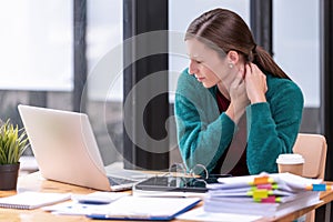 Young businesswoman office worker suffering from neck pain, massaging her neck at office table workplace, feeling overworked