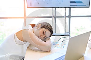 Young businesswoman overworked sleeping with laptop computer on desk in the office. Tired business Asian woman from working