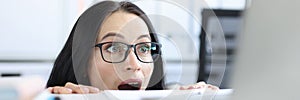 Young businesswoman peering over her desk in office in wide eyed horror or amazement