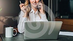 Young businesswoman in shirt is sitting in office at table in front of computer, talking on cell phone