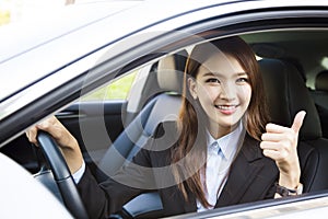 Young businesswoman sitting in car and showing thumbs up