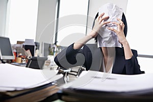 Young businesswoman sitting at desk covering her face with a paper