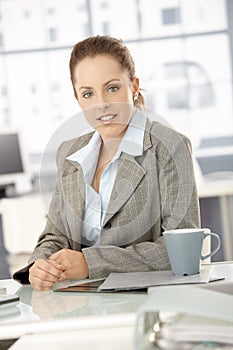 Young businesswoman sitting by desk in office