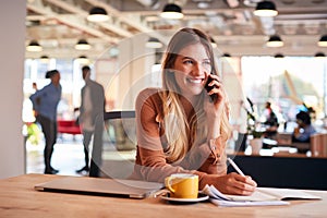 Young Businesswoman Sitting At Desk On Phone Call In Modern Open Plan Office